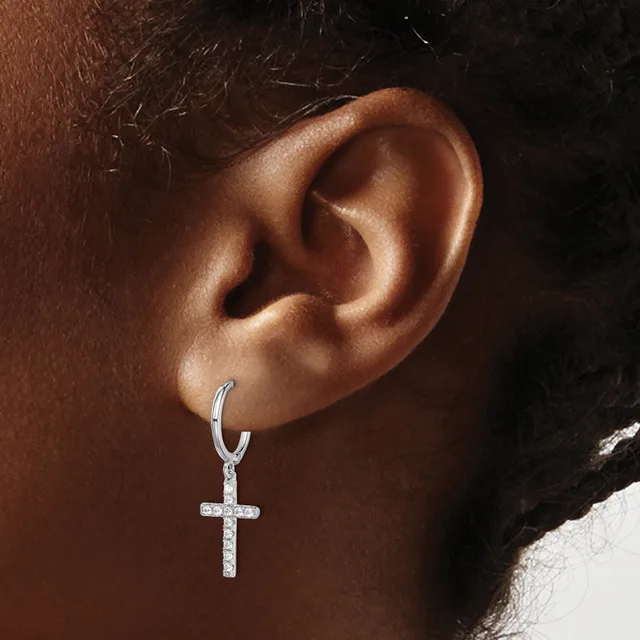 A person wearing a silver hoop earring with a dangling cross pendant studded with small crystals or diamonds.