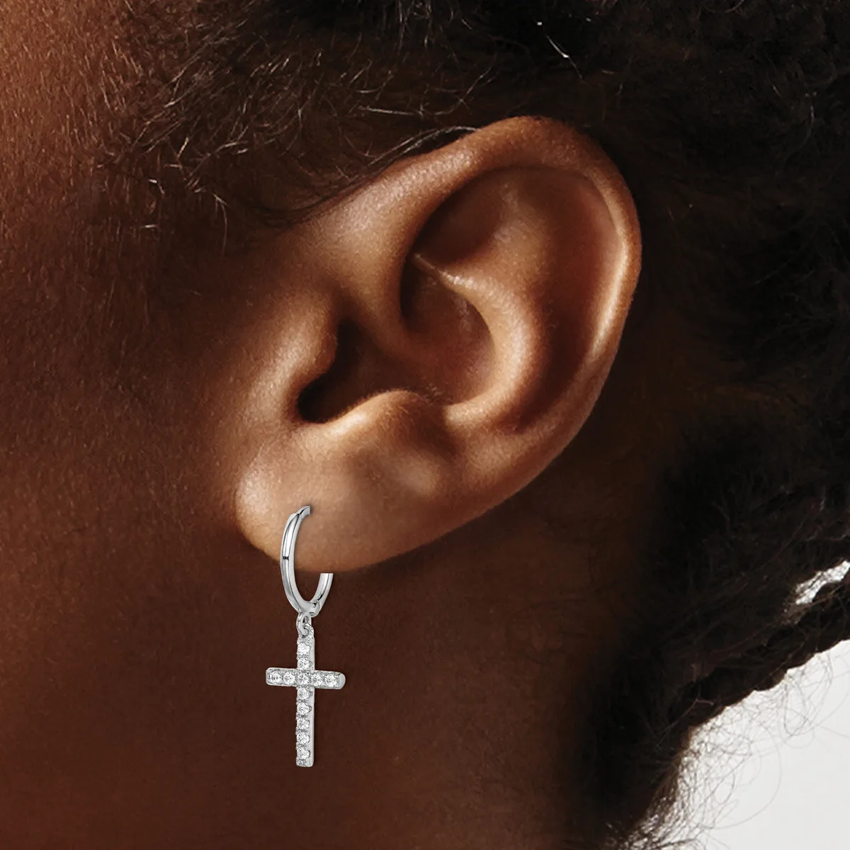 A person wearing a silver hoop earring with a dangling cross pendant studded with small crystals or diamonds.