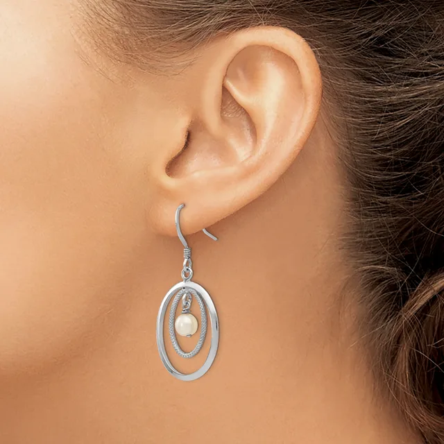 A silver-toned oval dangle earring with concentric ovals and a center pearl, shown worn on a model's ear.