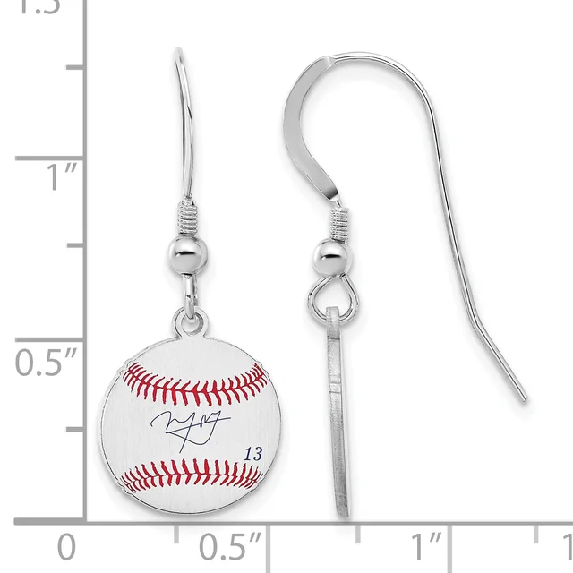 A pair of silver-toned baseball earrings with red stitching detail and a signature, suspended from curved wire hooks, shown against a measurement scale.