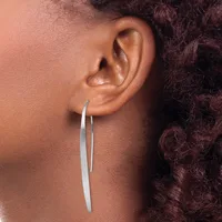 A person wearing long, curved silver earrings that extend downward from pierced earlobes, shown in profile against their neck and shoulder.