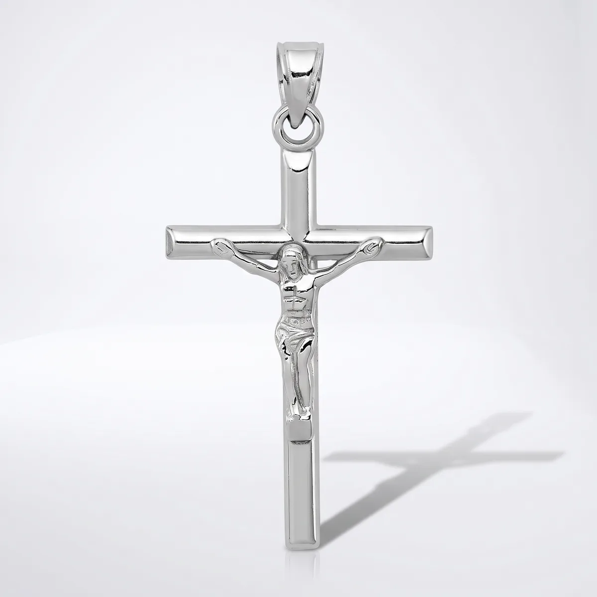 A silver crucifix pendant with a polished finish, featuring a detailed corpus figure, shown against a white background with a shadow visible to the right.