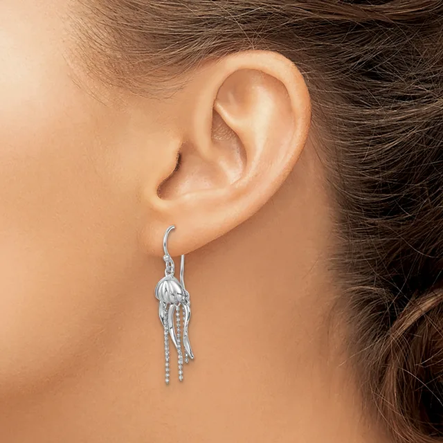 A woman wearing a dangling silver earring with a textured shell-like top and delicate beaded chains hanging below, shown from the side profile of her ear and neck.