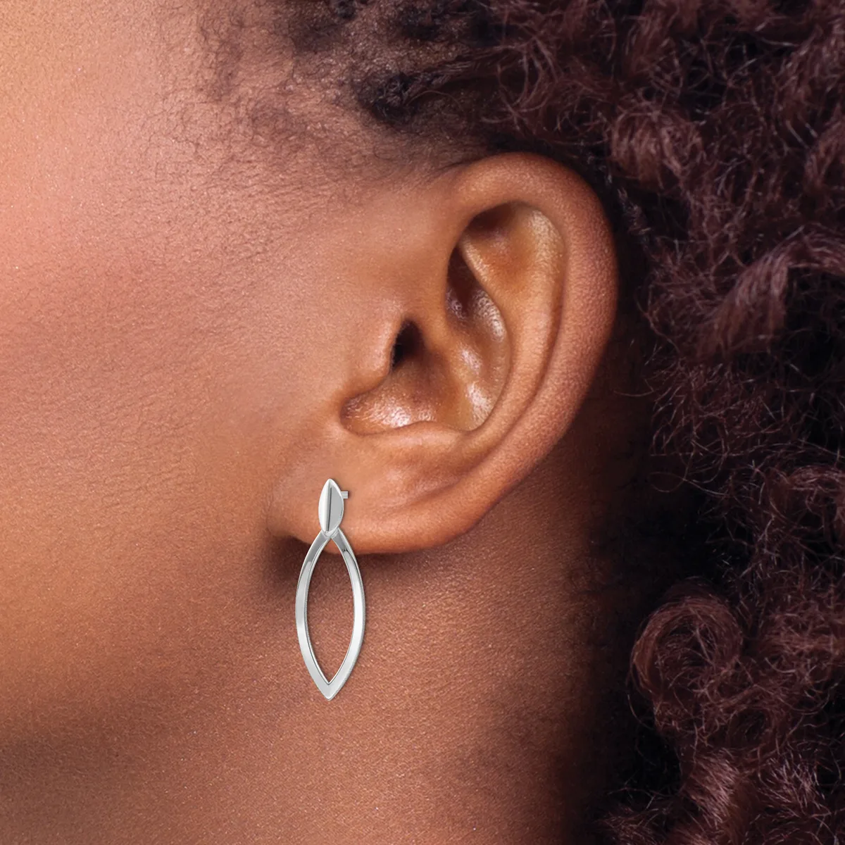 A person wearing a silver oval hoop earring, shown in profile against their ear and dark curly hair.