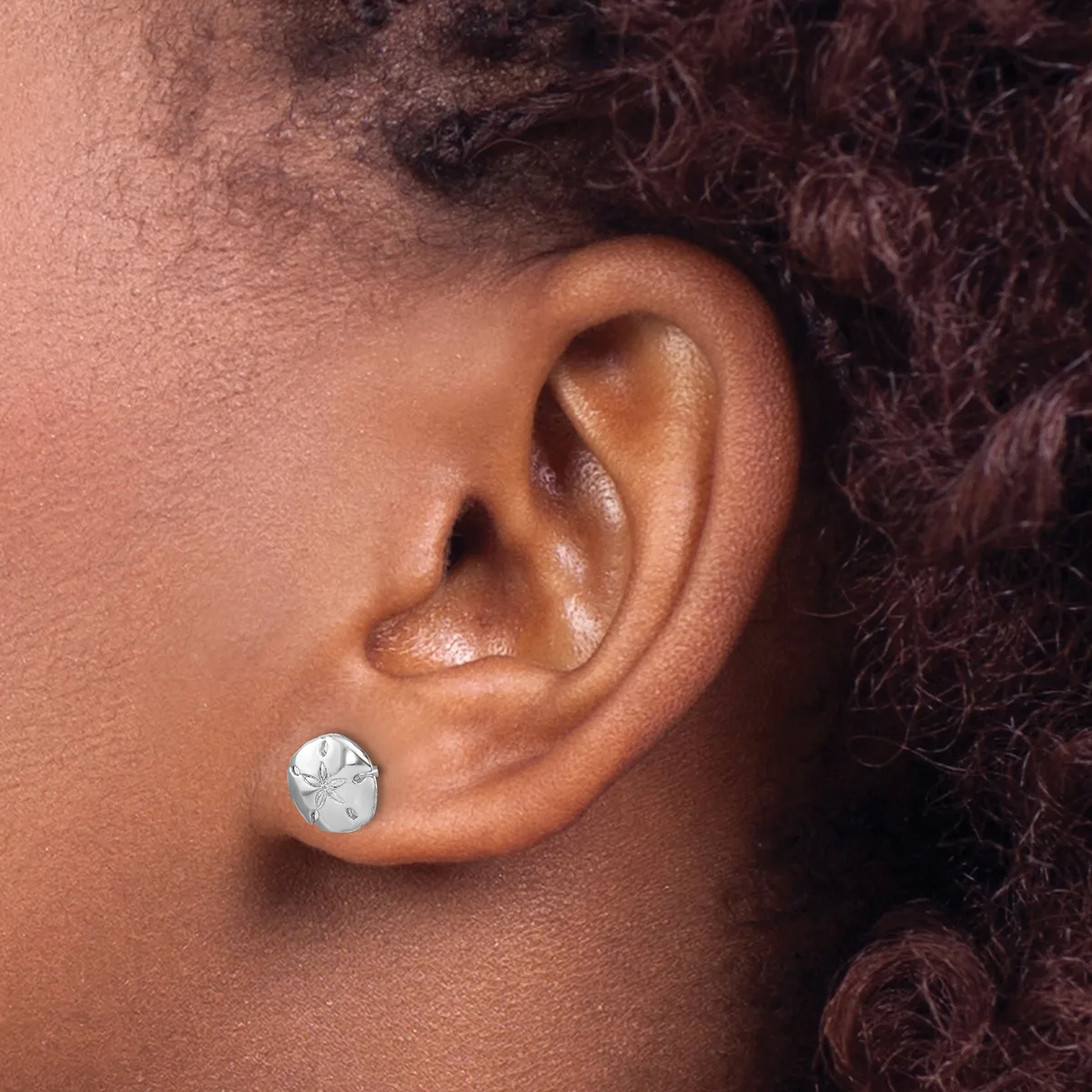 A person wearing a small round silver stud earring with a textured surface in their earlobe.