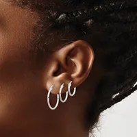 A person's ear displaying three silver hoop earrings of graduated sizes arranged in the earlobe area against brown skin and dark hair.