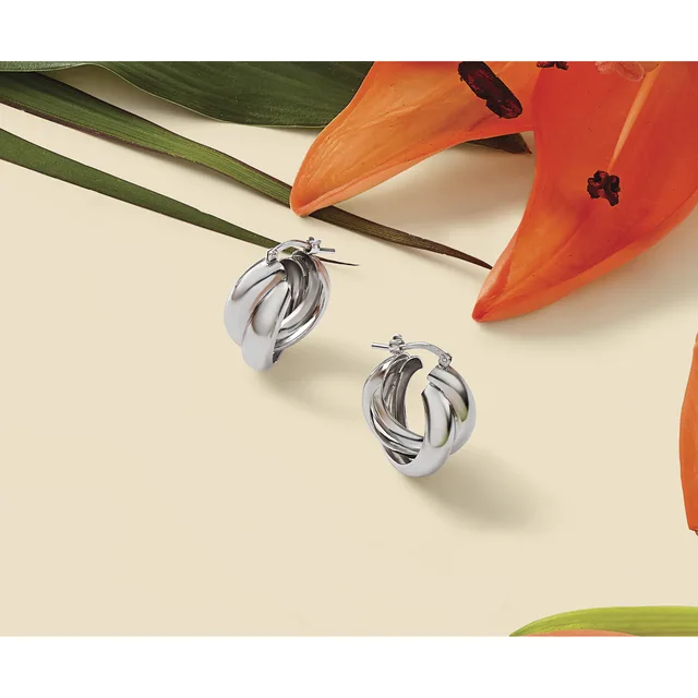 Two twisted silver hoop earrings displayed on a cream background with orange lilies and green leaves.