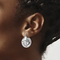 A silver circular drop earring with horizontal linear details worn on a person's ear against a brown skin tone.
