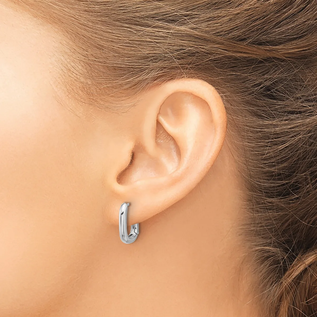 A person wearing a small silver hoop earring in their earlobe, shown from the side profile of their ear and neck.