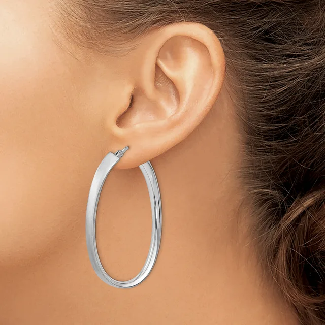 A person wearing a pair of polished silver oval hoop earrings, shown from the side view of their ear and neck.