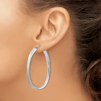 A person wearing a pair of polished silver oval hoop earrings, shown from the side view of their ear and neck.