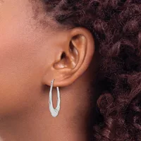 A person wearing a pair of polished silver-toned oval hoop earrings, shown from the side profile view.