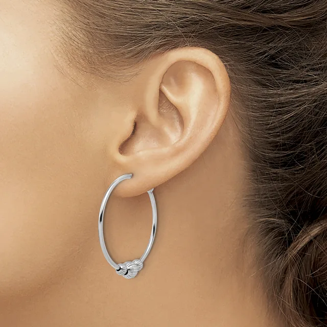 A person wearing a silver oval hoop earring with a decorative clasp, shown from the side view of their ear and neck.