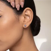 A woman wearing a blue and white stud earring in her earlobe, with dark hair pulled back and pale pink nail polish on her fingernails.