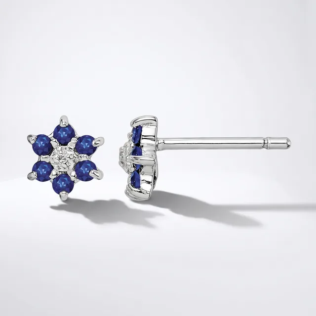 A pair of white metal stud earrings featuring blue gemstones arranged in a flower pattern with a small diamond or crystal in the center, shown from front and back views.
