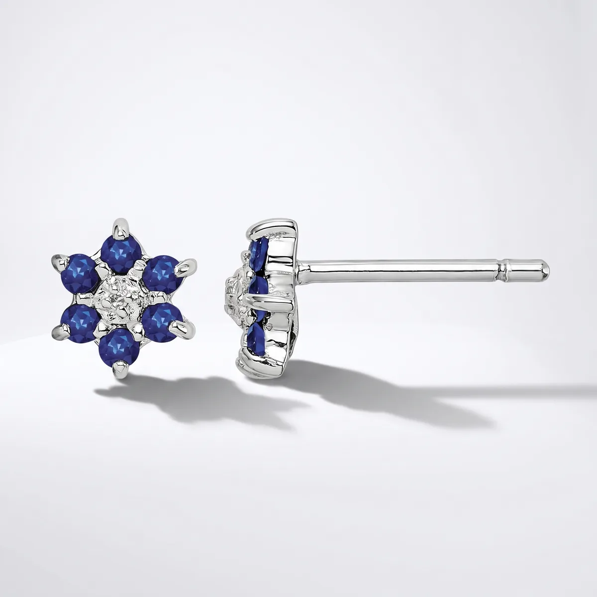 A pair of white metal stud earrings featuring blue gemstones arranged in a flower pattern with a small diamond or crystal in the center, shown from front and back views.