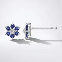 A pair of white metal stud earrings featuring blue gemstones arranged in a flower pattern with a small diamond or crystal in the center, shown from front and back views.