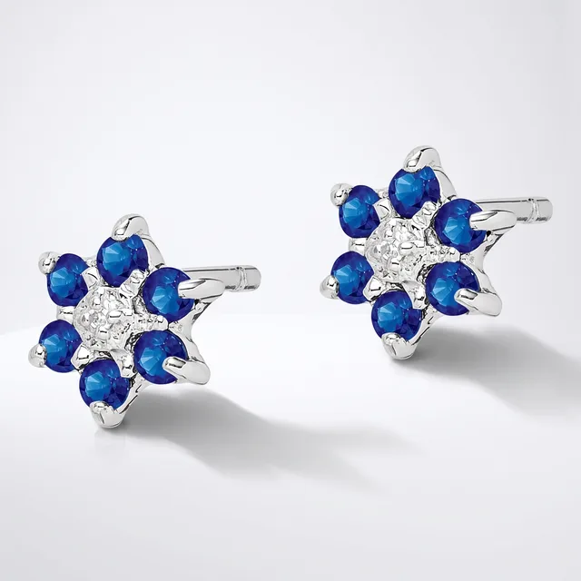 A pair of silver star-shaped stud earrings, each featuring a central cluster of white diamonds surrounded by eight blue sapphires in a flower pattern.