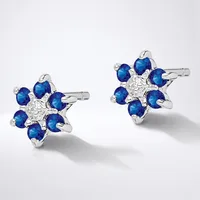 A pair of silver star-shaped stud earrings, each featuring a central cluster of white diamonds surrounded by eight blue sapphires in a flower pattern.