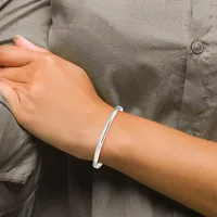 A person wearing a gray button-up shirt displays a polished silver bangle bracelet on their wrist.