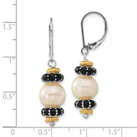 A pair of earrings with cream-colored pearl drops separated by black ridged beads and gold-toned spacers, suspended from leverback closures, shown against a measurement scale.