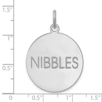 A polished silver-toned round pendant with the word "NIBBLES" engraved on its surface, shown against a measurement scale.