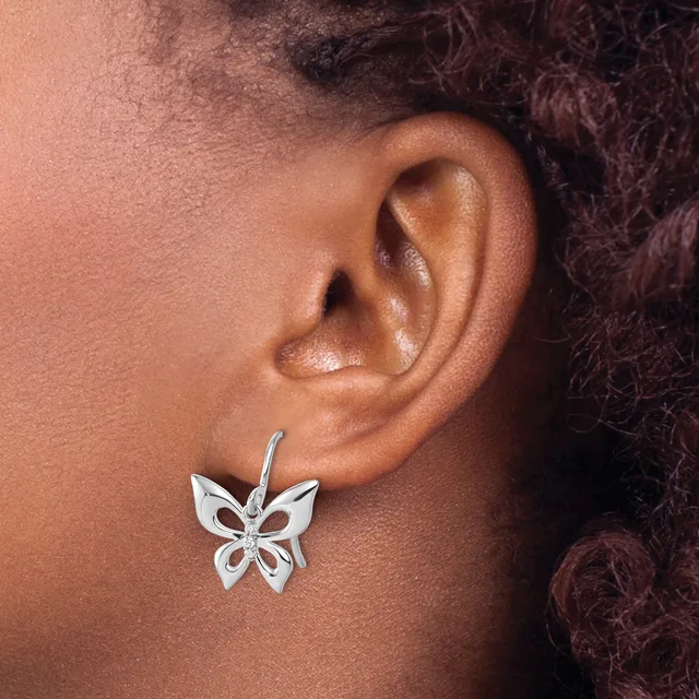 A silver butterfly-shaped earring with open-work design and a small round stone in the center hangs from an ear lobe.