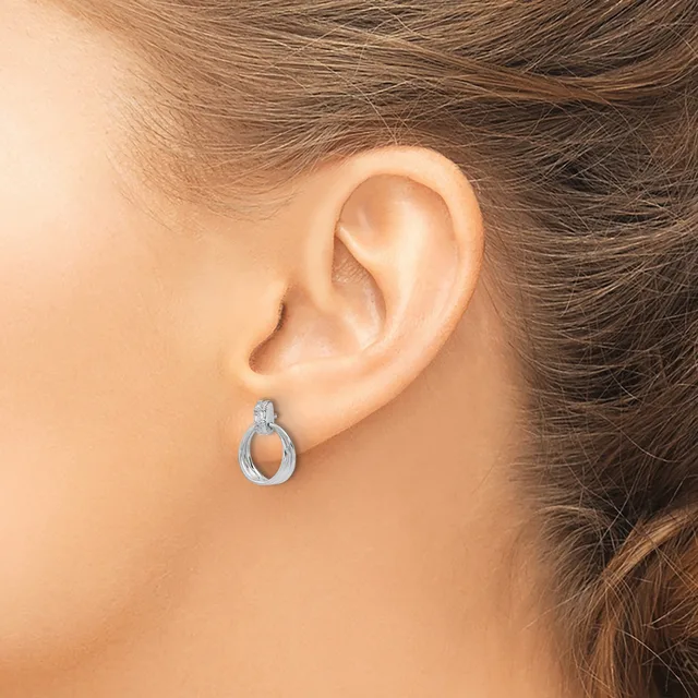 A woman wearing a small silver teardrop-shaped hoop earring with a textured finish, shown from the side view of her ear.