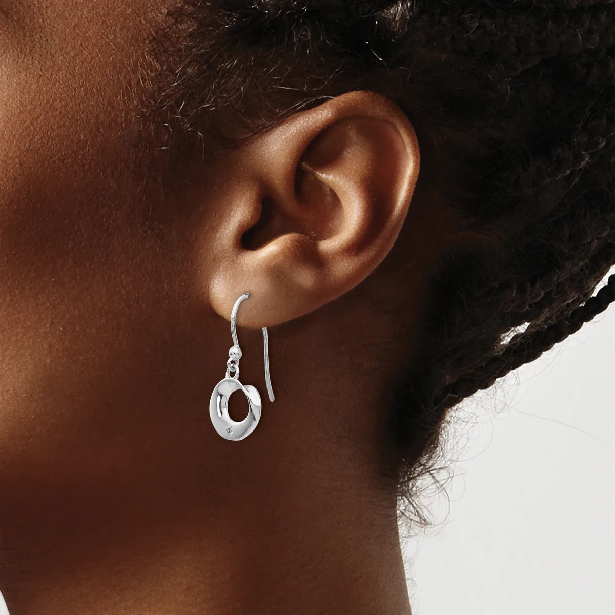 A person wearing a silver hook earring with a small circular pendant hanging from their earlobe.