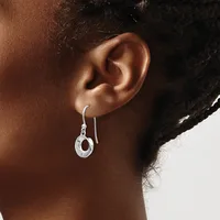 A person wearing a silver hook earring with a small circular pendant hanging from their earlobe.