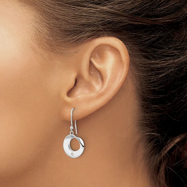A silver drop earring with a circular open design hangs from a hook, worn on a person's earlobe.