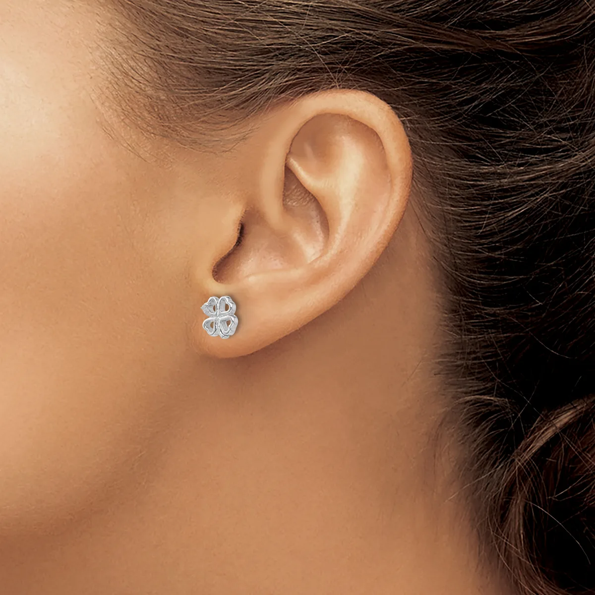 A person wearing a small silver four-leaf clover stud earring in their pierced earlobe, shown in close-up profile view.
