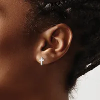A person wearing a small silver cross earring in their earlobe, shown in profile against a neutral background.