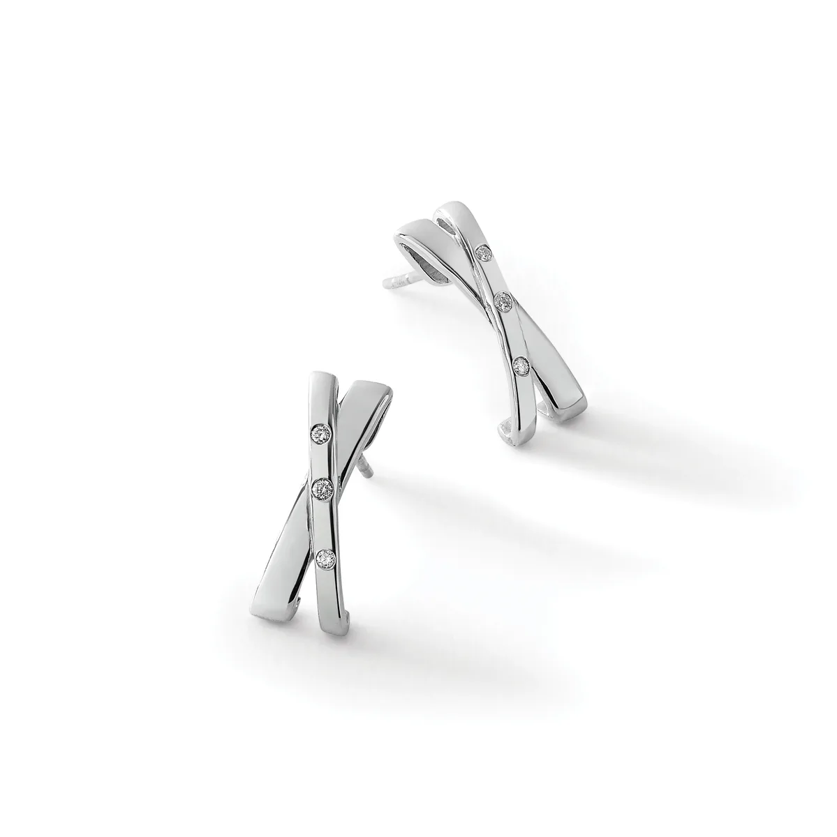 Two silver crossover earrings with small round diamond accents, displayed at angles on a white surface.