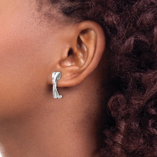 A person wearing a silver curved cuff earring in their pierced earlobe, shown in profile view against their shoulder and dark curly hair.