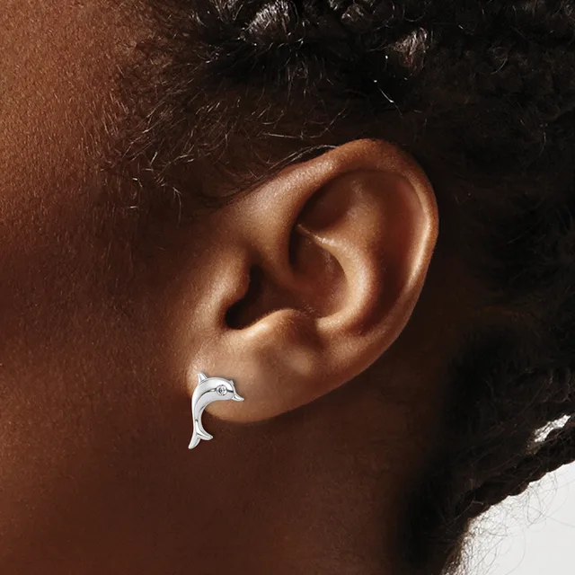 A silver crescent-shaped earring worn in a person's earlobe, shown in profile against their brown skin tone.