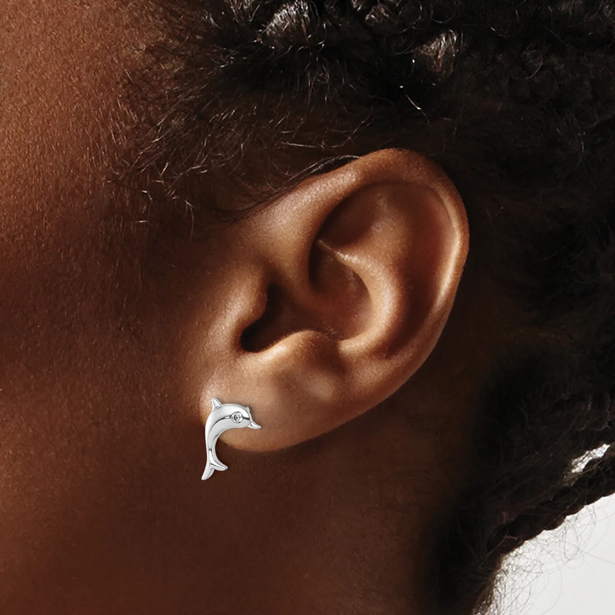 A silver crescent-shaped earring worn in a person's earlobe, shown in profile against their brown skin tone.