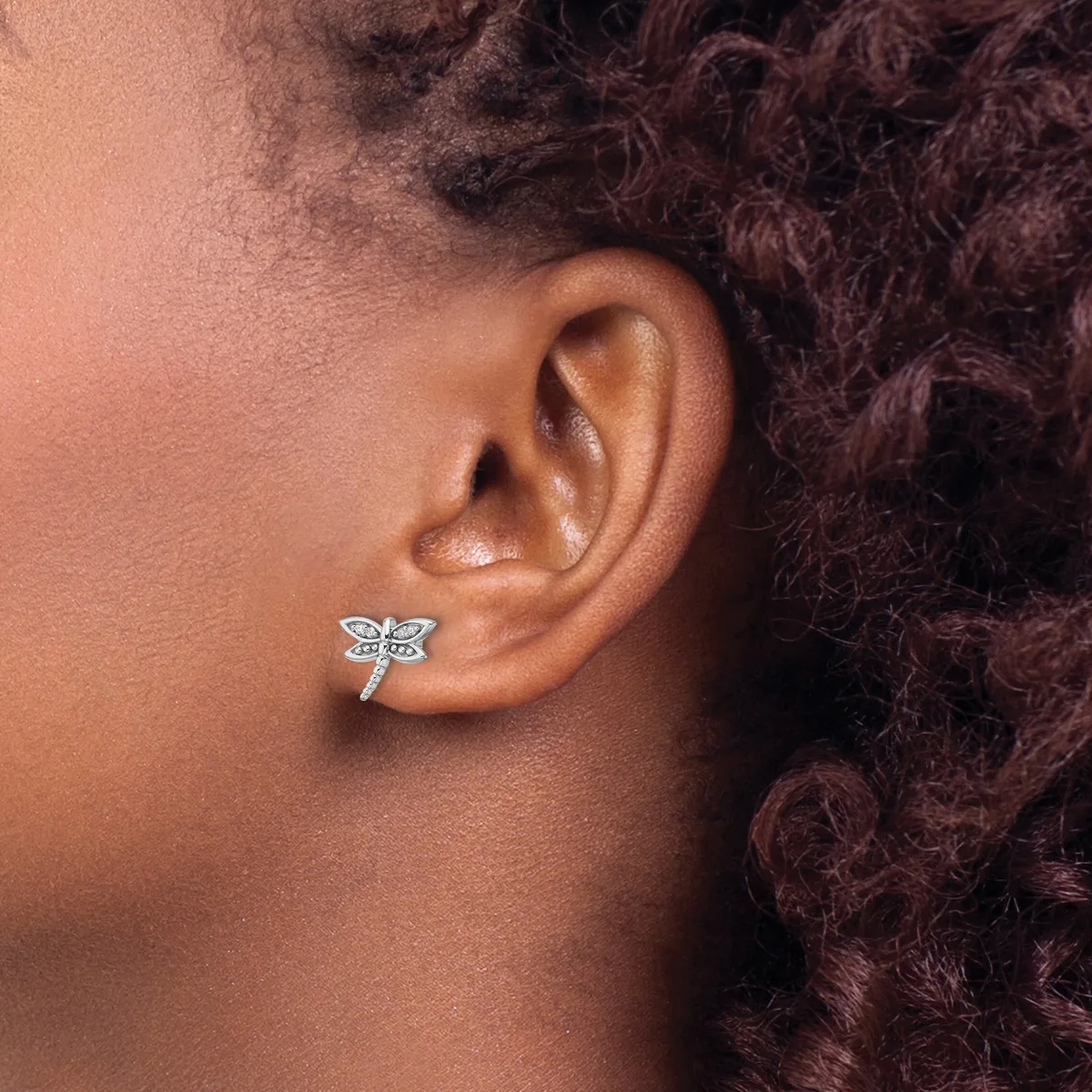 A person wearing a small silver dragonfly stud earring in their earlobe, shown in profile against their neck and shoulder.