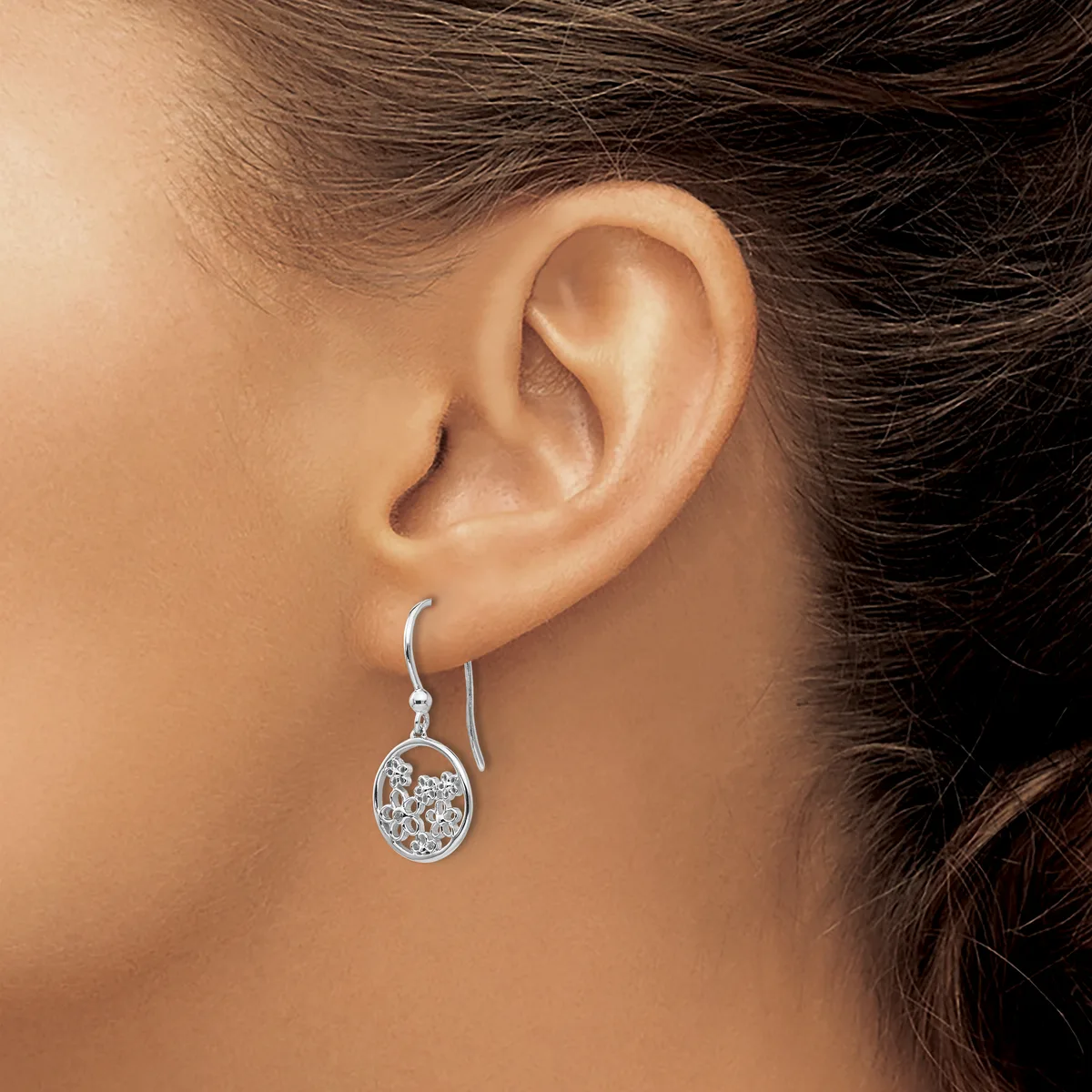 A woman wearing a silver drop earring with a circular pendant containing small sparkling stones, shown from the side view against her ear.