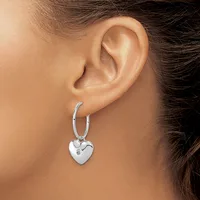 A person wearing silver hoop earrings with a dangling heart-shaped pendant set with a small clear stone, shown from the side against their ear.