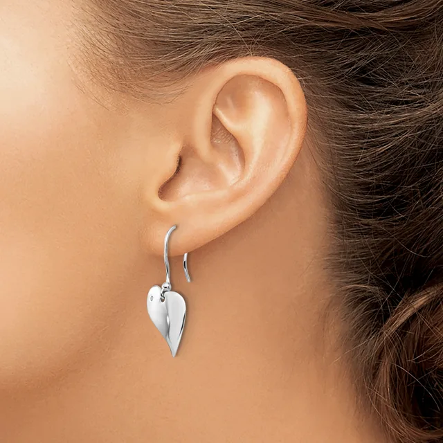A person wearing silver leaf-shaped drop earrings on hook posts, shown from the side profile of their ear and neck.
