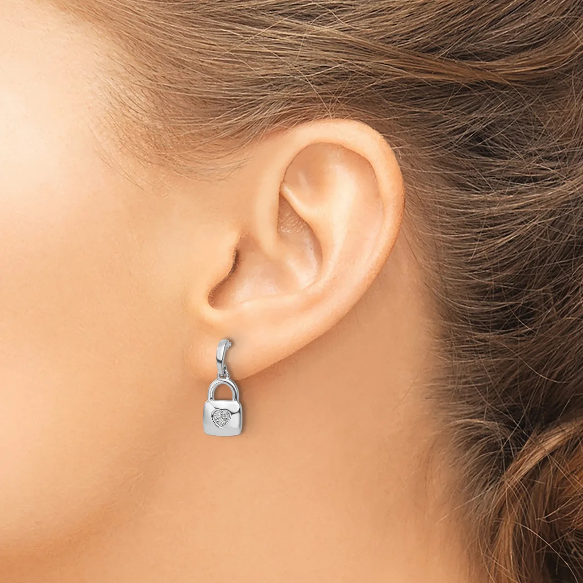 A woman wearing a silver handbag-shaped dangle earring with a small heart detail, shown from the side profile of her ear.
