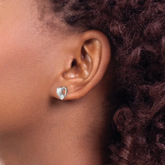 A person wearing a small silver heart-shaped stud earring with a polished finish in their pierced earlobe, shown in profile view.