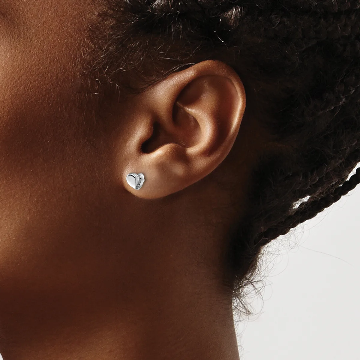A person with dark hair and brown skin wearing a small silver heart-shaped stud earring in their earlobe, shown in profile against a white background.