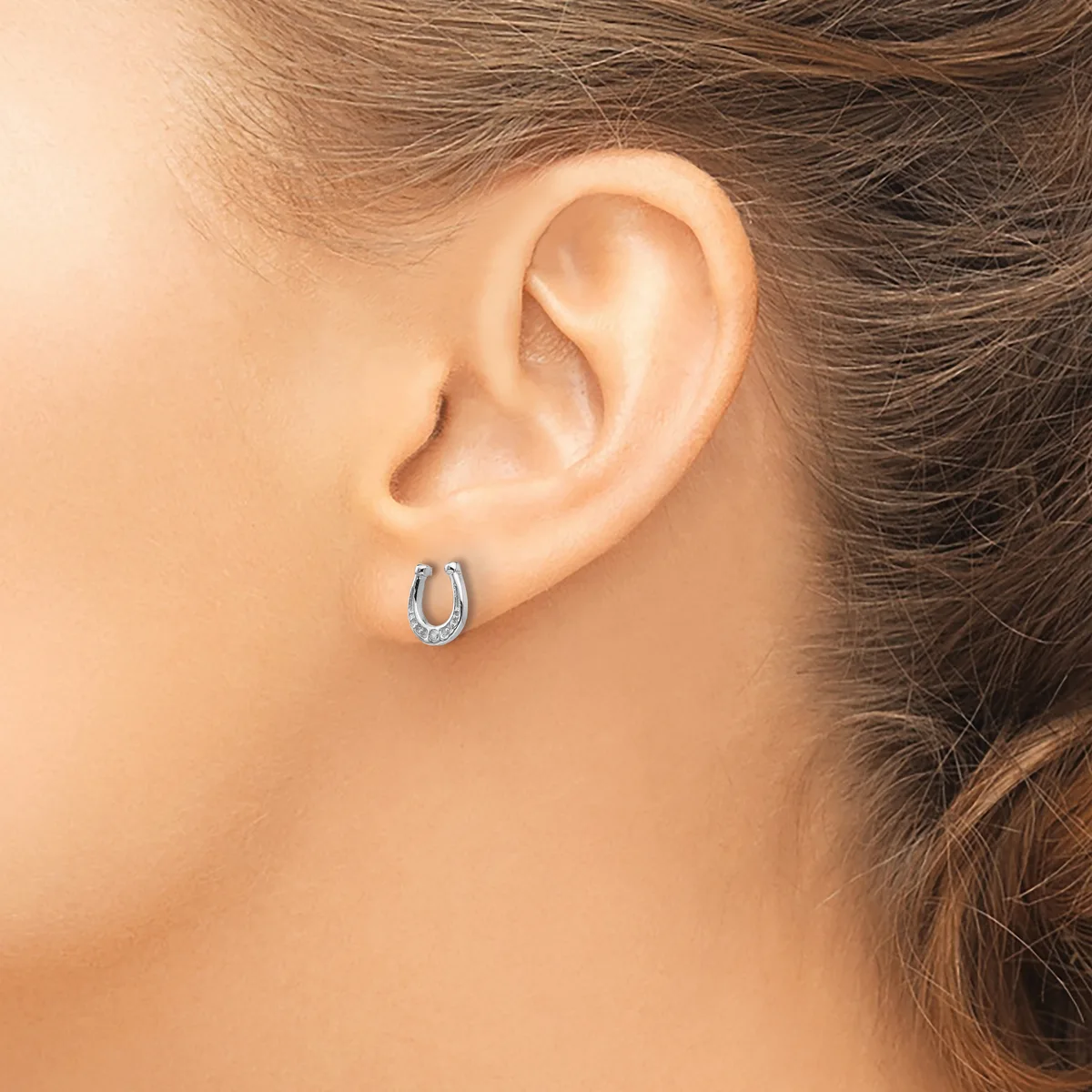 A person wearing small silver hoop earrings with a textured surface, shown from the side view of their ear and neck.