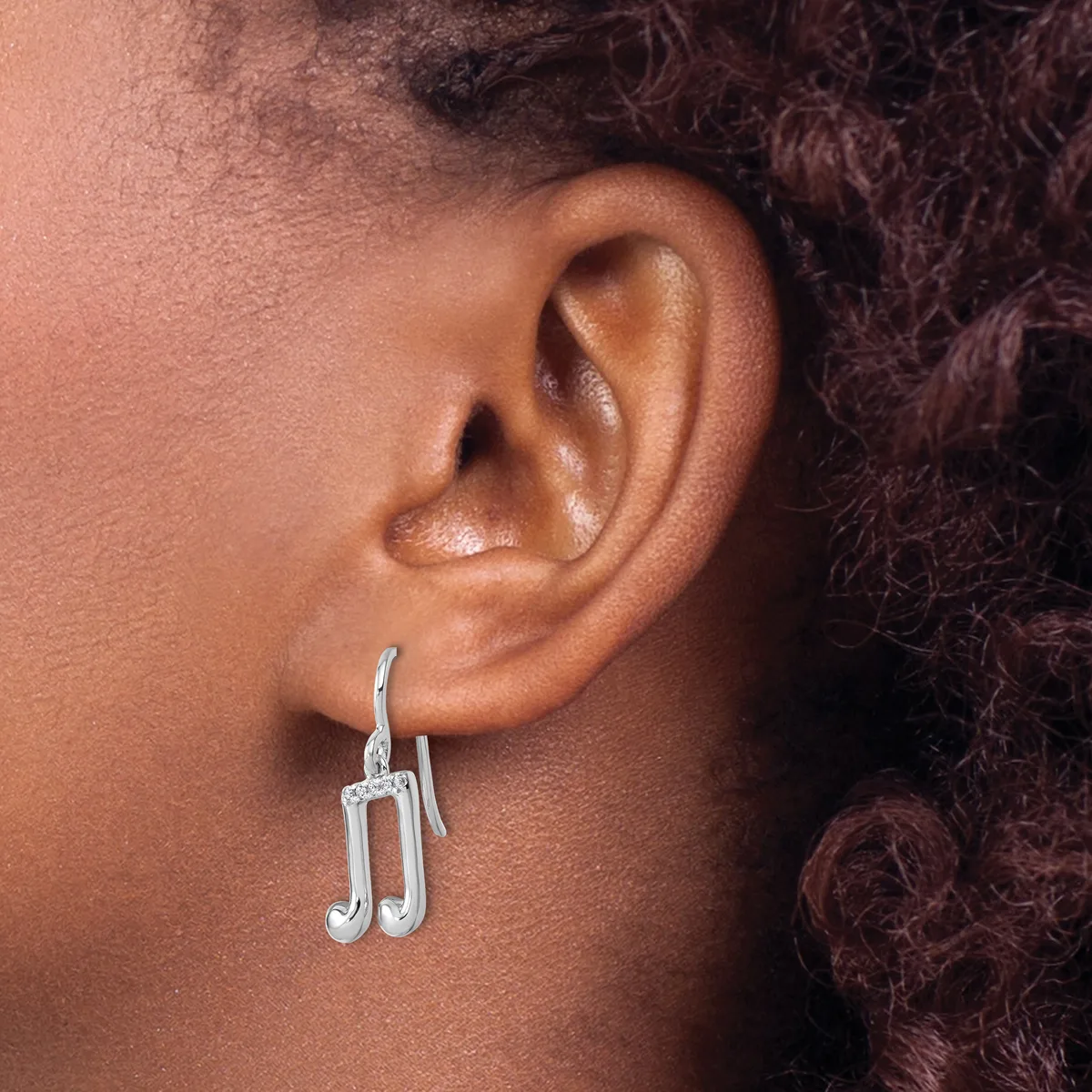 A person wearing silver musical note-shaped drop earrings, shown from the side profile with dark curly hair visible.