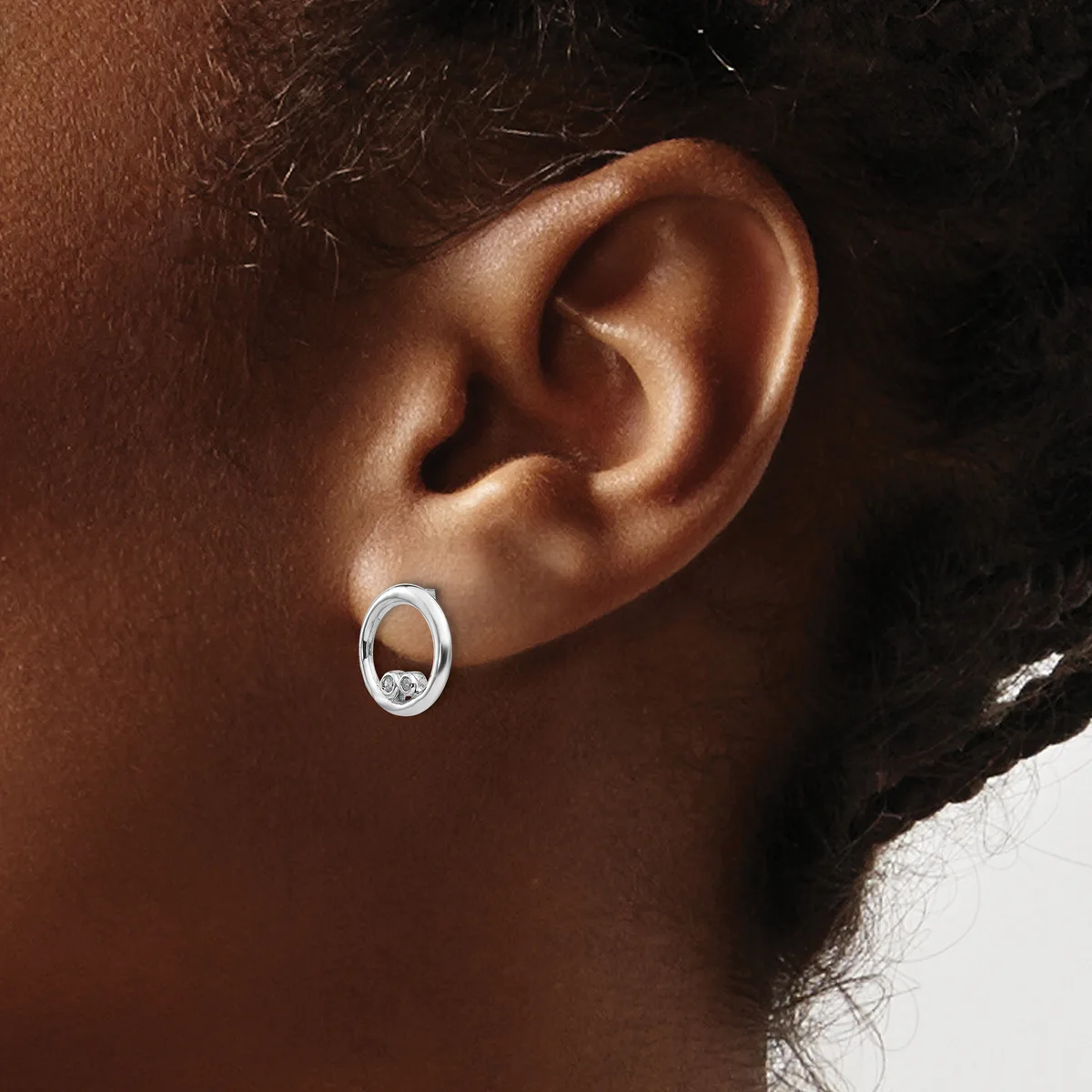 A close-up view of a person's ear wearing a small oval silver hoop earring with a decorative center detail.