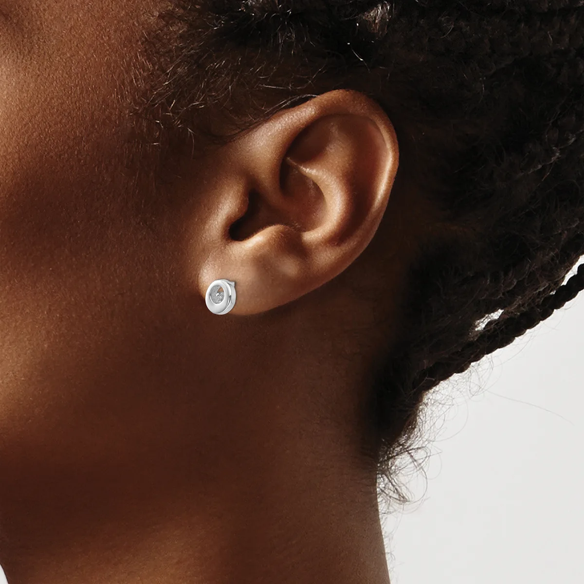 A person wearing a small oval silver stud earring with a blue stone or enamel center, shown from the side view of their ear and neck.
