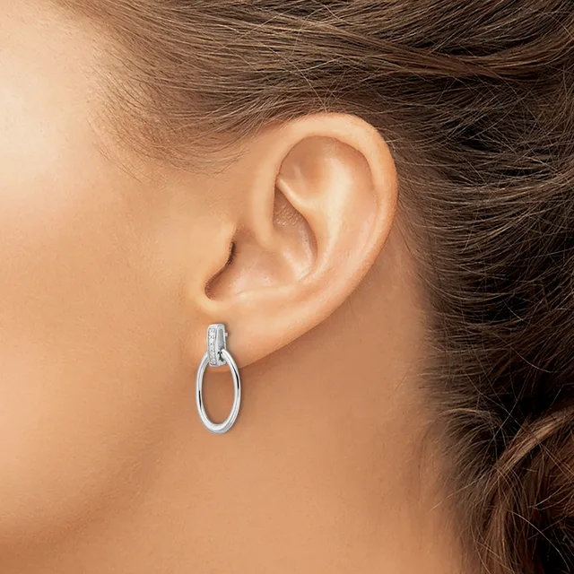 A woman wearing a small silver oval hoop earring with a textured top section, shown from the side view of her ear and neck.