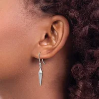 A person wearing a silver drop earring with an elongated pointed pendant hanging from a curved wire hook, shown from the side view against their ear.